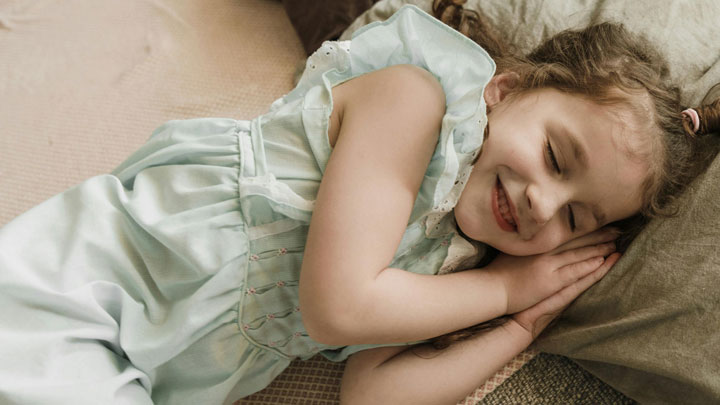 A young girl with her eyes closed and a big smile on her face, lying in bed and not sleeping.