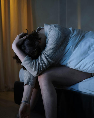 A teenage boy sitting on a bed with a thoughtful expression, holding his head in his hands, illustrating bipolar disorder in teenagers.