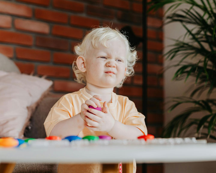 A toddler sitting on the floor, hugging a pile of toys protectively, illustrating the difficulty in sharing toys often experienced at this age.