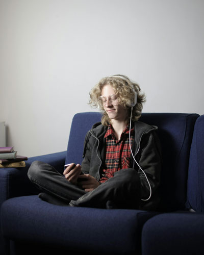 A teenage boy sitting on a couch, engrossed in his smartphone, illustrating excessive use of digital media.