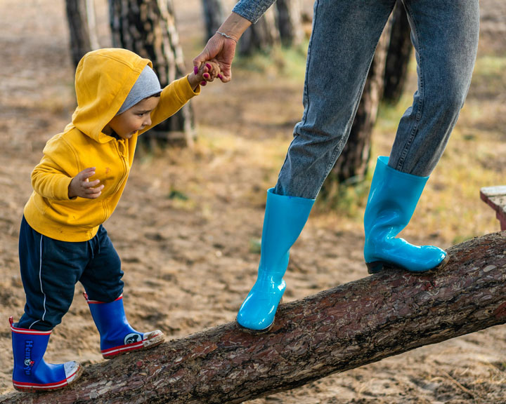 A toddler balancing on a wooden log with the help of her mother, illustrating the importance of focusing in toddlers as they develop motor skills and concentration.