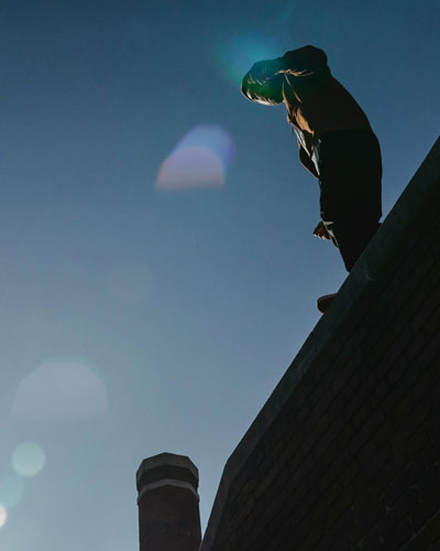 A teenage boy standing on a high wall, looking down, illustrating risky behaviors in teenagers.